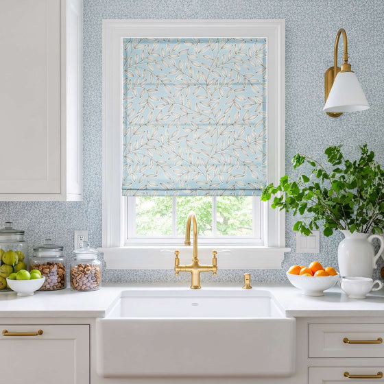 Blue,Kitchen with a window featuring a floral patterned roller blind, white sink, and countertop with fruits and a plant.