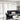 White,Living room with a gray sofa, white curtains, and a small table with decor items.