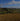 Hilly landscape with a mix of green and brown fields under a blue sky with clouds.